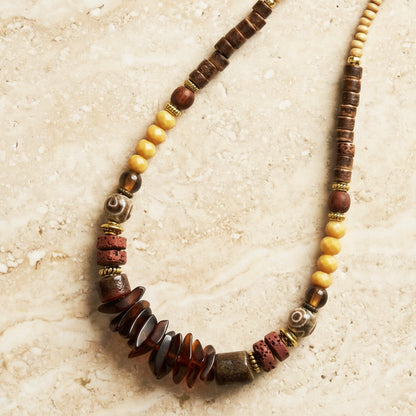 Beaded necklace with brown, yellow, and red beads on a textured beige surface