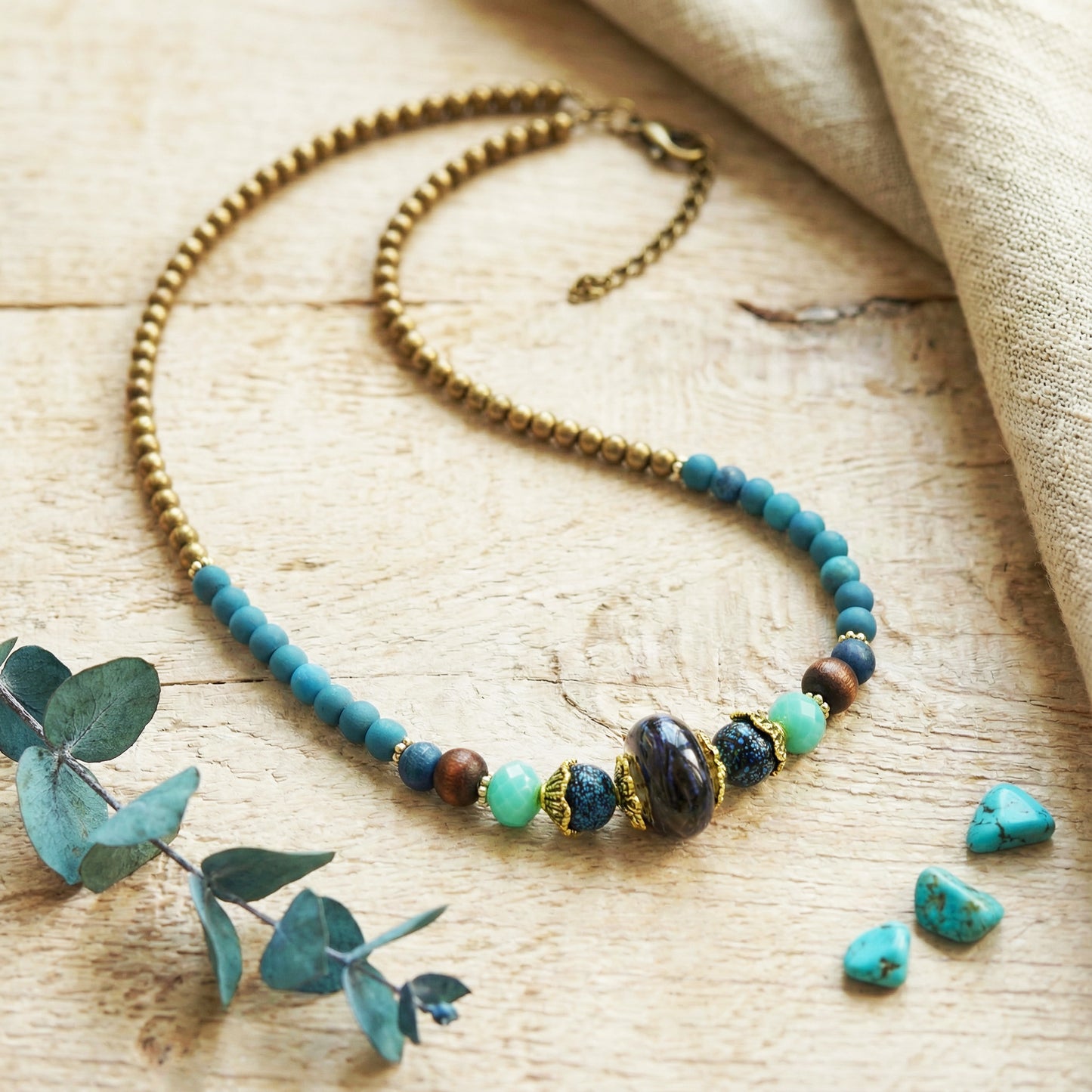 Necklace with blue and brown beads on a wooden surface with eucalyptus leaves.