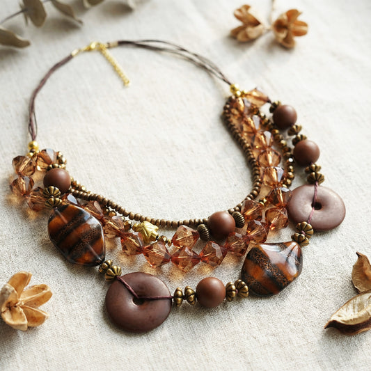 Necklace with brown and gold beads on a textured surface with dried flowers.