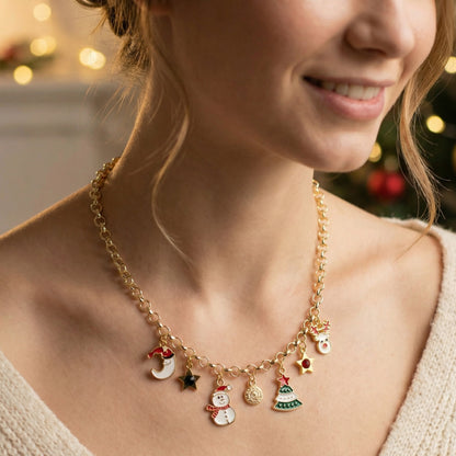 A gold-toned holiday charm necklace worn by a woman, featuring small enamel charms including a snowman, Christmas tree, moon, star, and Santa, with a warm festive background.