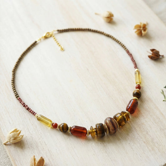 Necklace with brown and amber beads on a light wooden surface with dried flowers.
