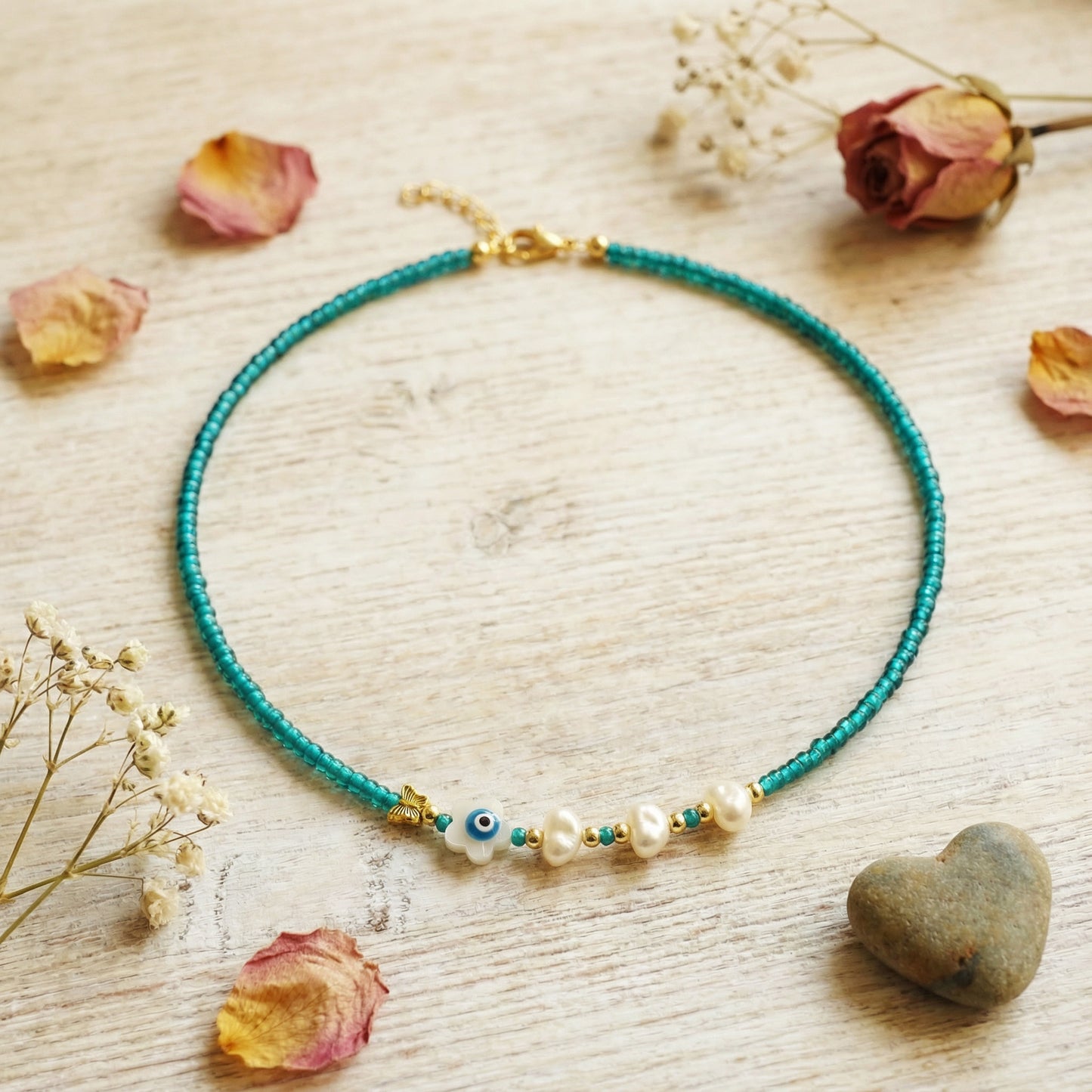 Necklace with blue beads and pearls on a wooden surface with dried flowers and a heart stone.
