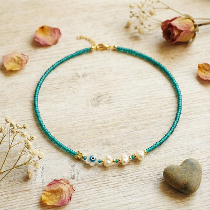 Necklace with blue beads and pearls on a wooden surface with dried flowers and a heart stone.