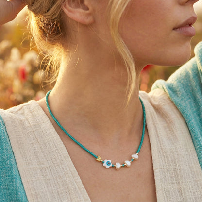 Close-up of a woman wearing a turquoise necklace with eye-shaped beads in an outdoor setting.