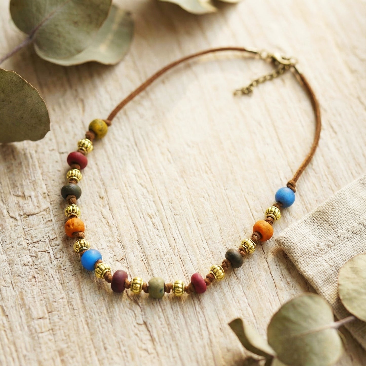 Necklace with colorful beads on a wooden surface with eucalyptus leaves