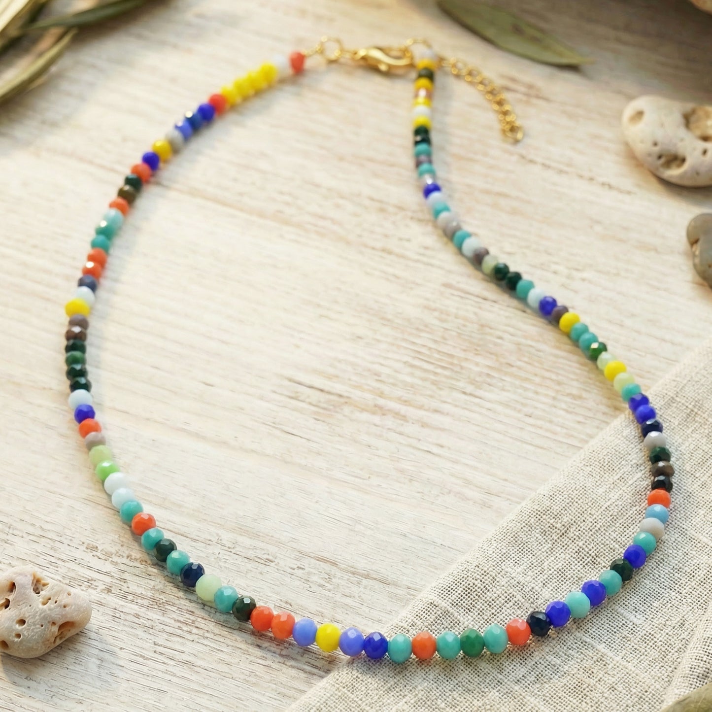 Colorful beaded necklace on a textured surface with natural elements.