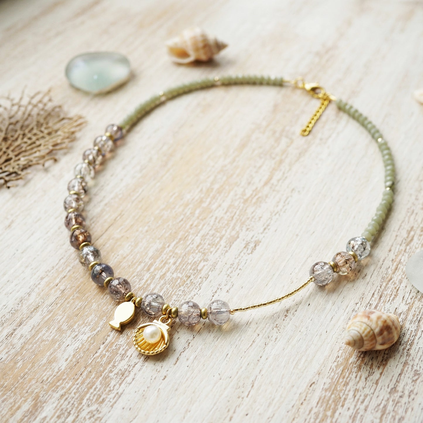 Necklace with shell and pearl charms on a wooden surface with shells