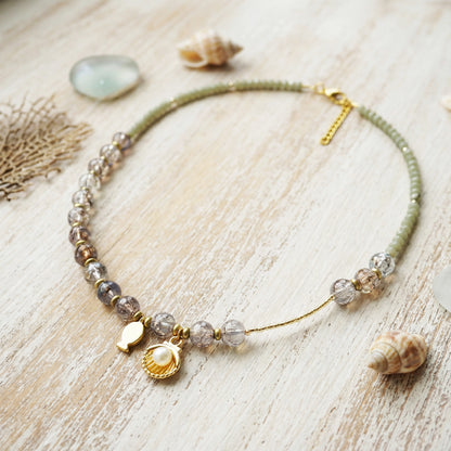 Necklace with shell and pearl charms on a wooden surface with shells