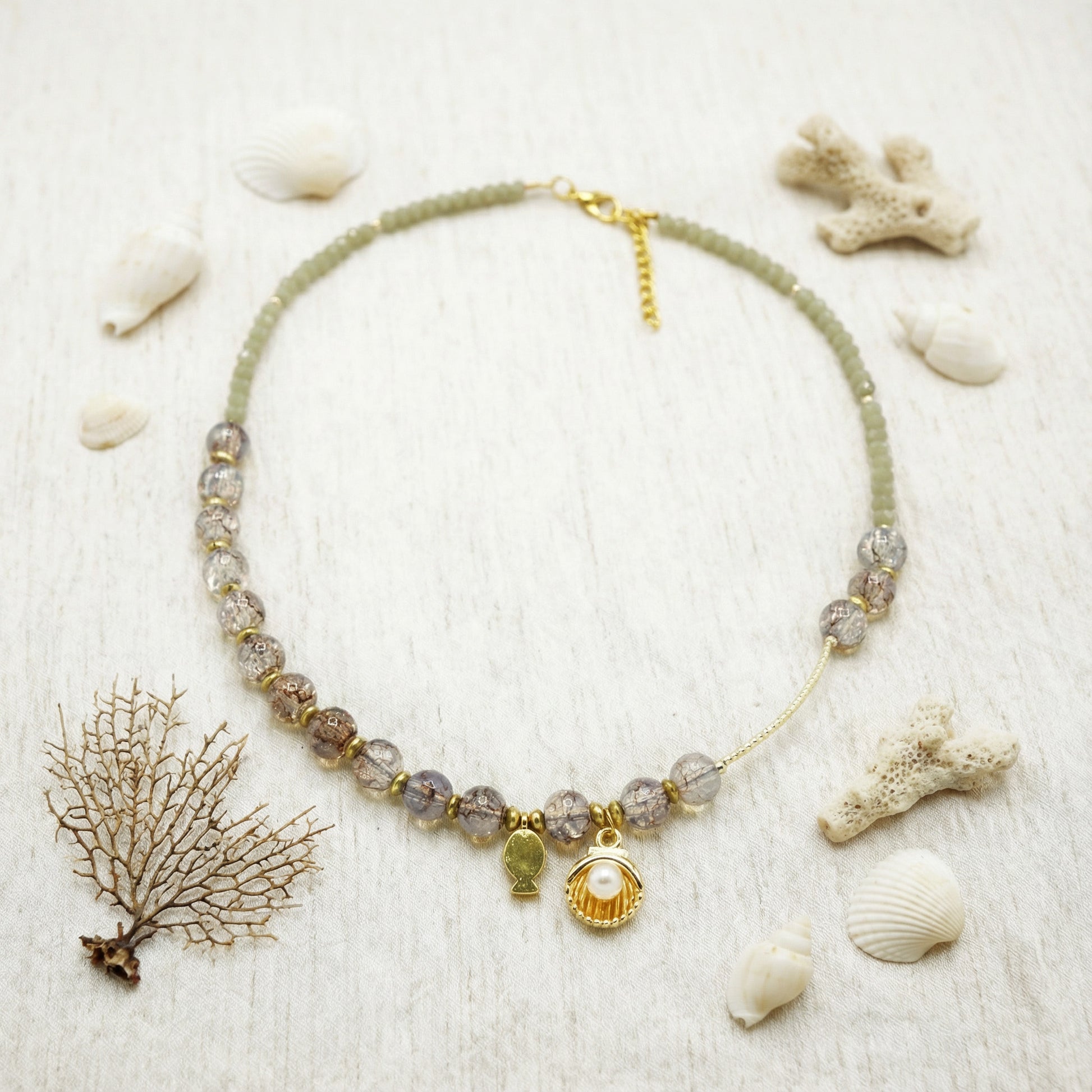 Necklace with shell charm on a sandy background with shells and coral