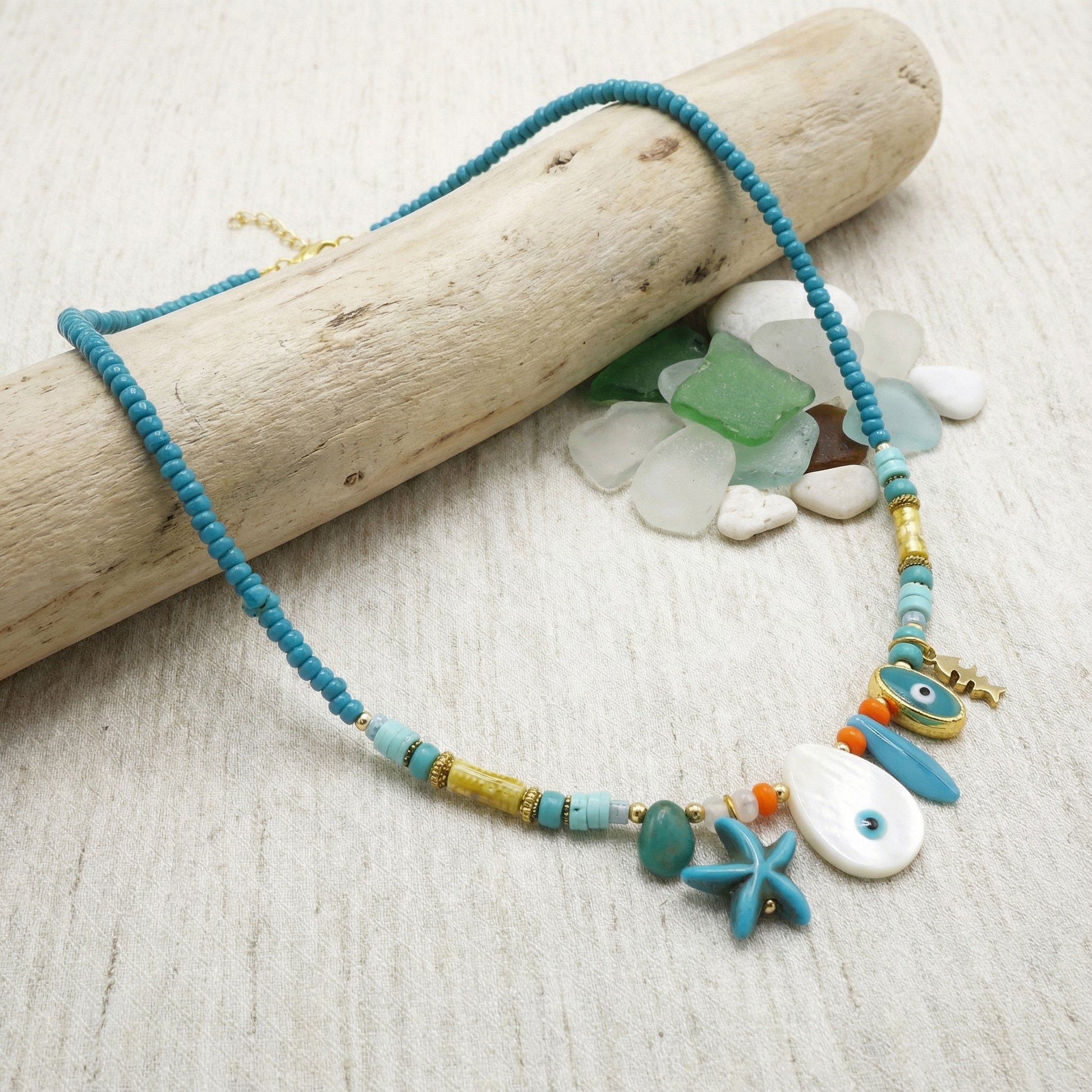 Necklace with blue and green beads and starfish charm on a wooden log and beach stones background