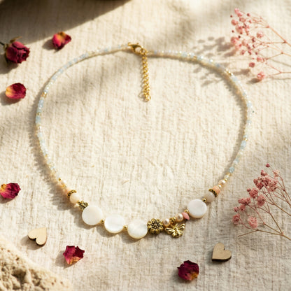 Necklace with heart and flower charms on a textured surface with dried flowers