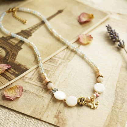Beaded necklace with white and gold elements on a textured surface with dried flowers and a vintage map.