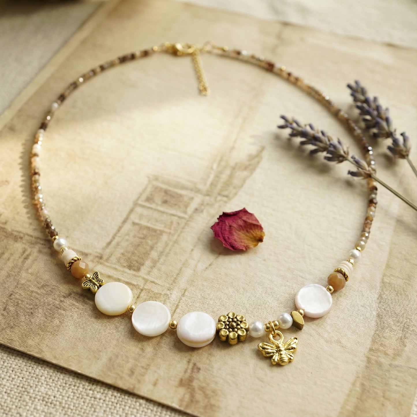 Necklace with white beads and gold accents on a textured surface with dried flowers.