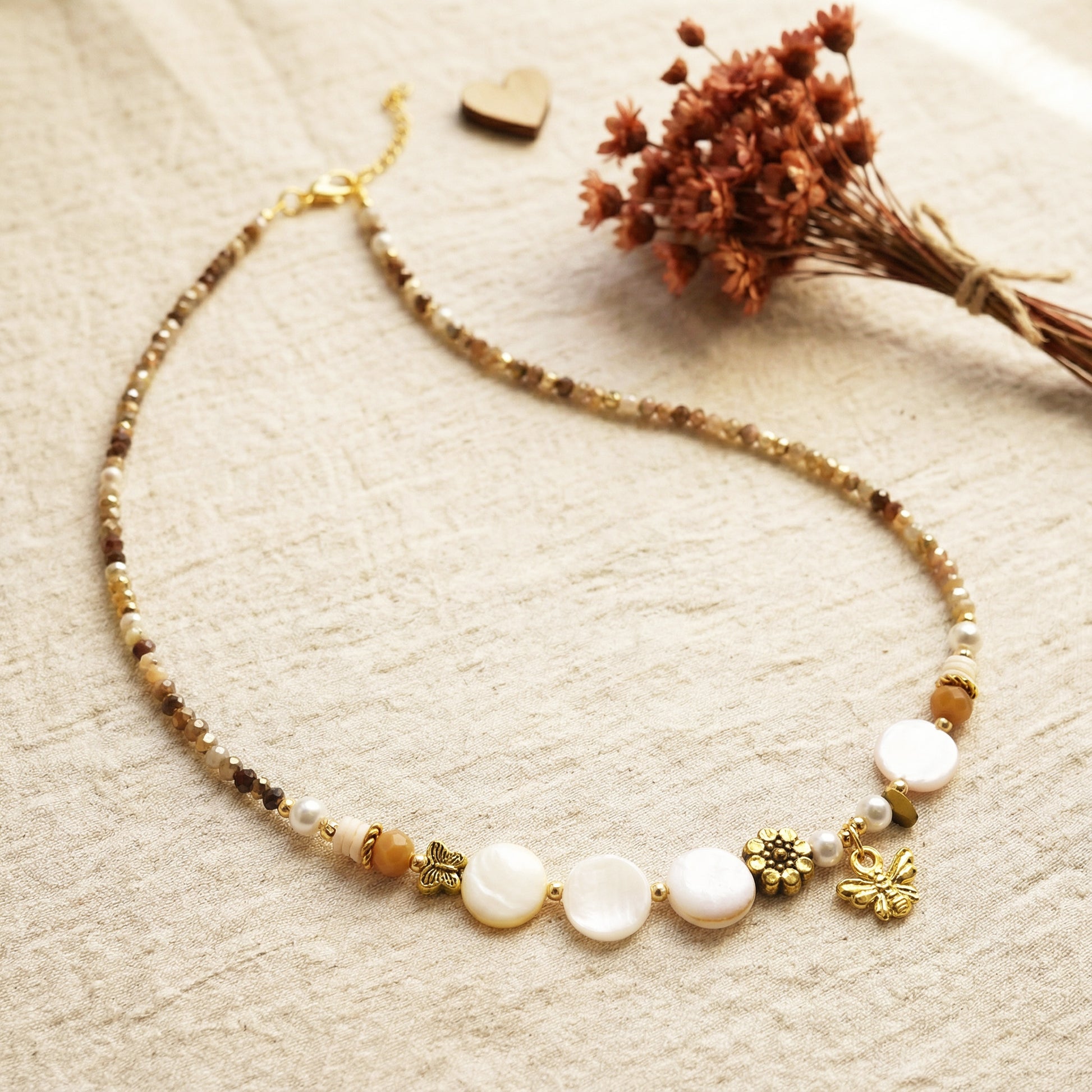 Necklace with beads and charms on a textured surface with dried flowers