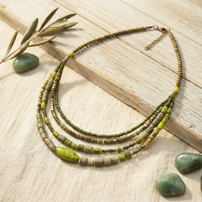 Necklace with green and brown beads on a wooden surface with stones and leaves.