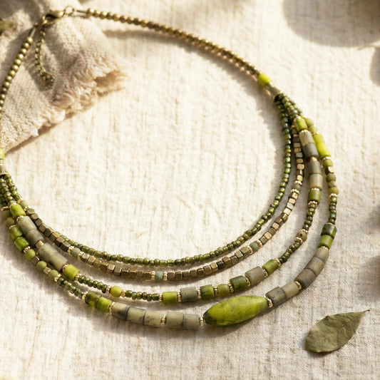 Green and beige beaded necklace on a textured fabric background