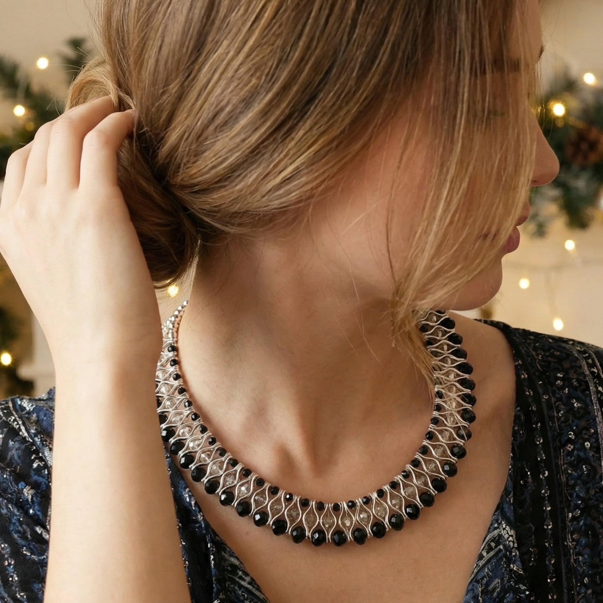 Woman wearing a black and silver beaded necklace with a blurred indoor background