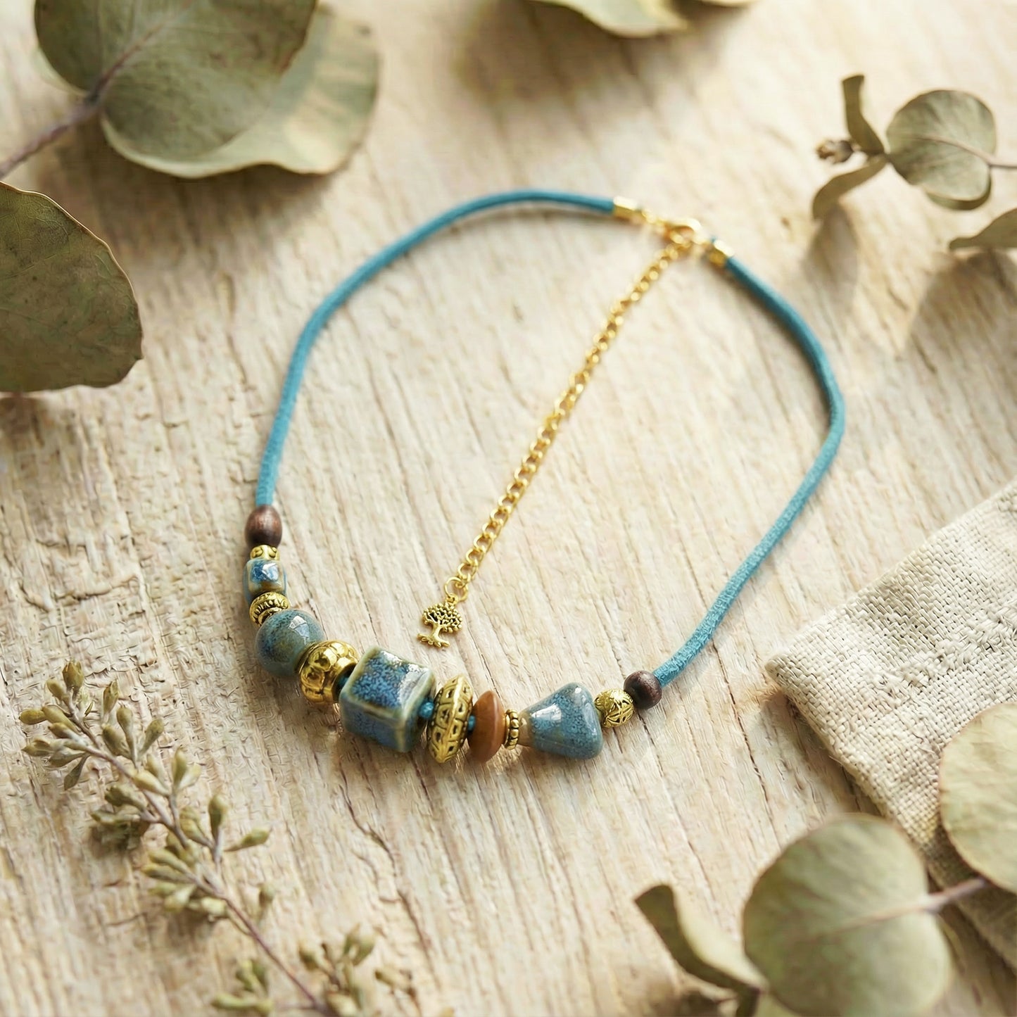 Necklace with blue cord and beaded elements on a wooden surface with eucalyptus leaves.
