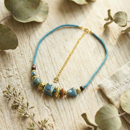 Necklace with blue cord and beaded elements on a wooden surface with eucalyptus leaves.