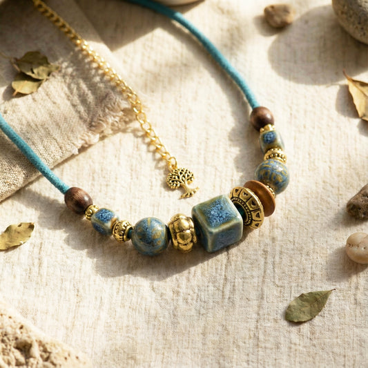 Necklace with blue and gold beads on a textured surface with leaves and stones.