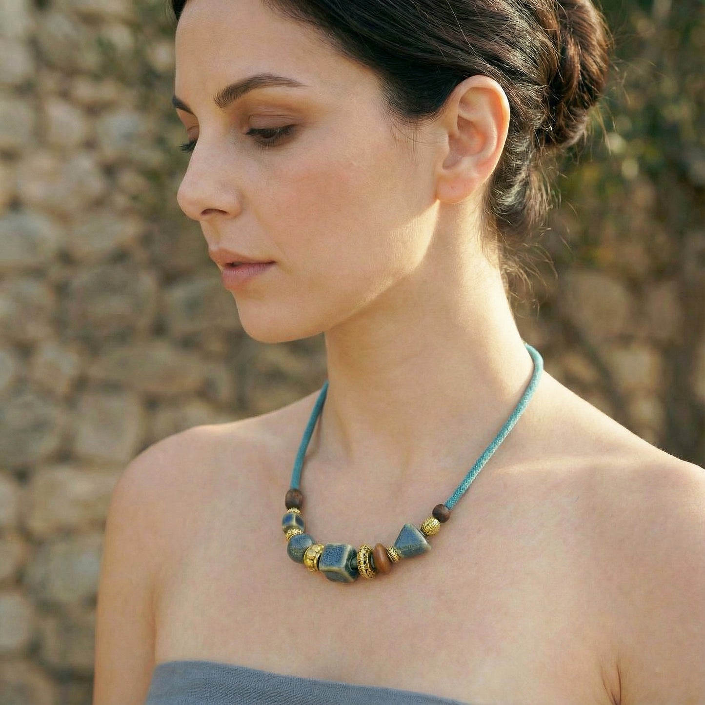 Woman wearing a blue beaded necklace against a stone wall background