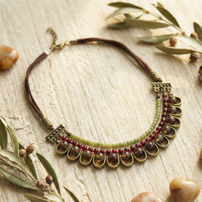 Necklace with beads and leather strap on a wooden surface with leaves and stones.