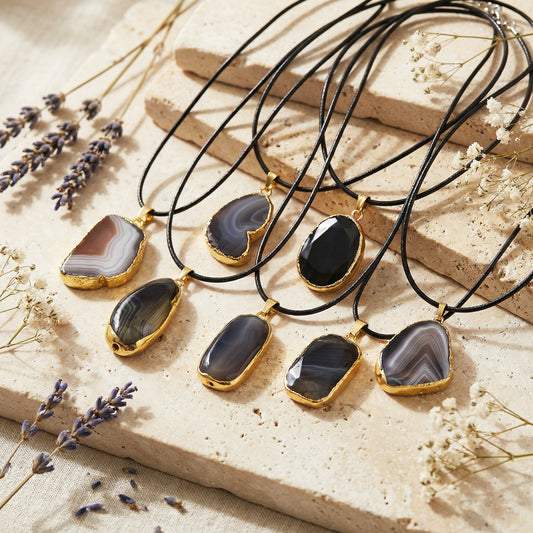 Necklaces with agate pendants on black cords, arranged on a textured surface with lavender and flowers.