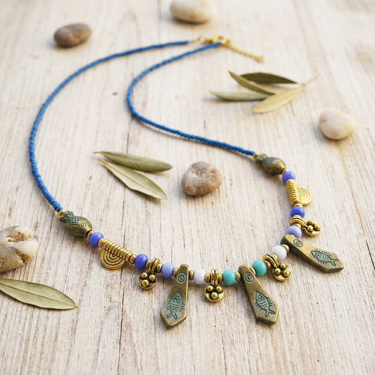 Necklace with blue cord and various beads on a wooden surface with leaves and stones.