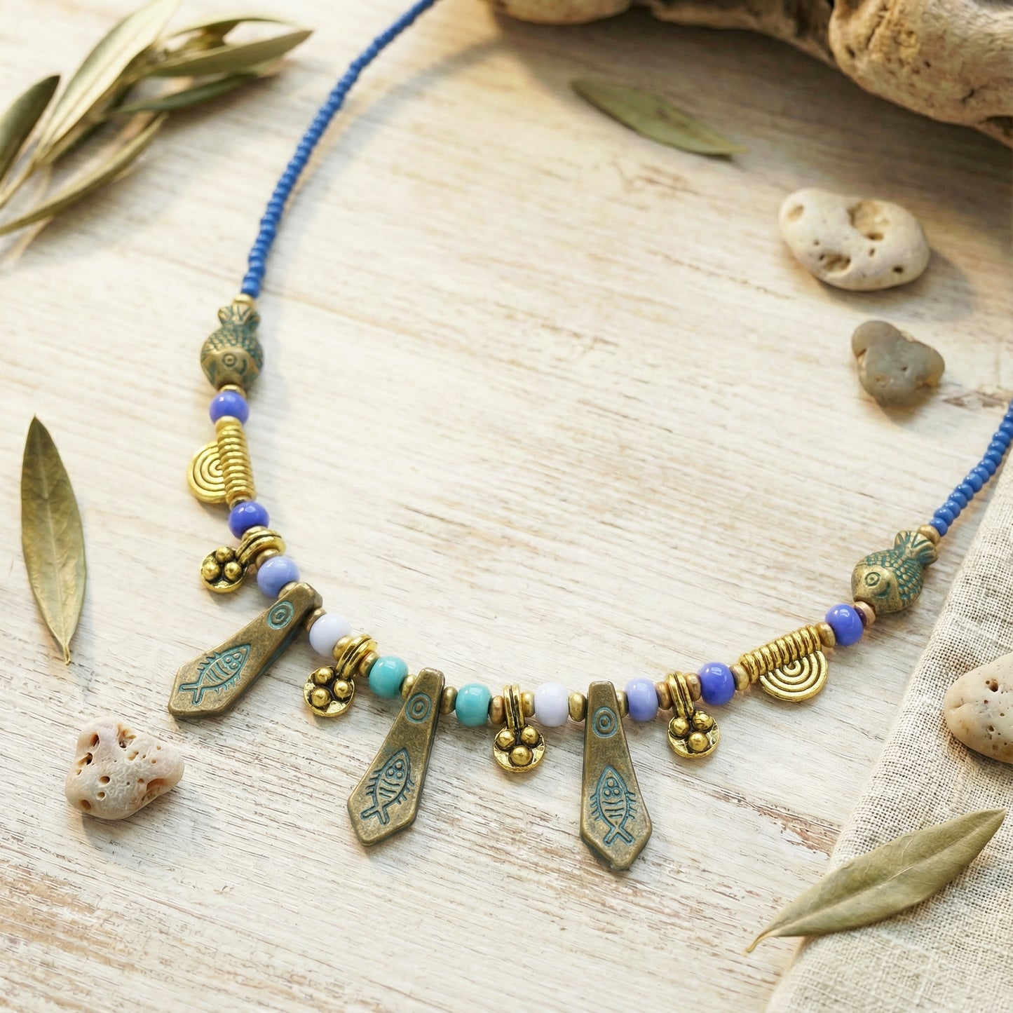 Necklace with gold and blue beads on a wooden surface with leaves and stones