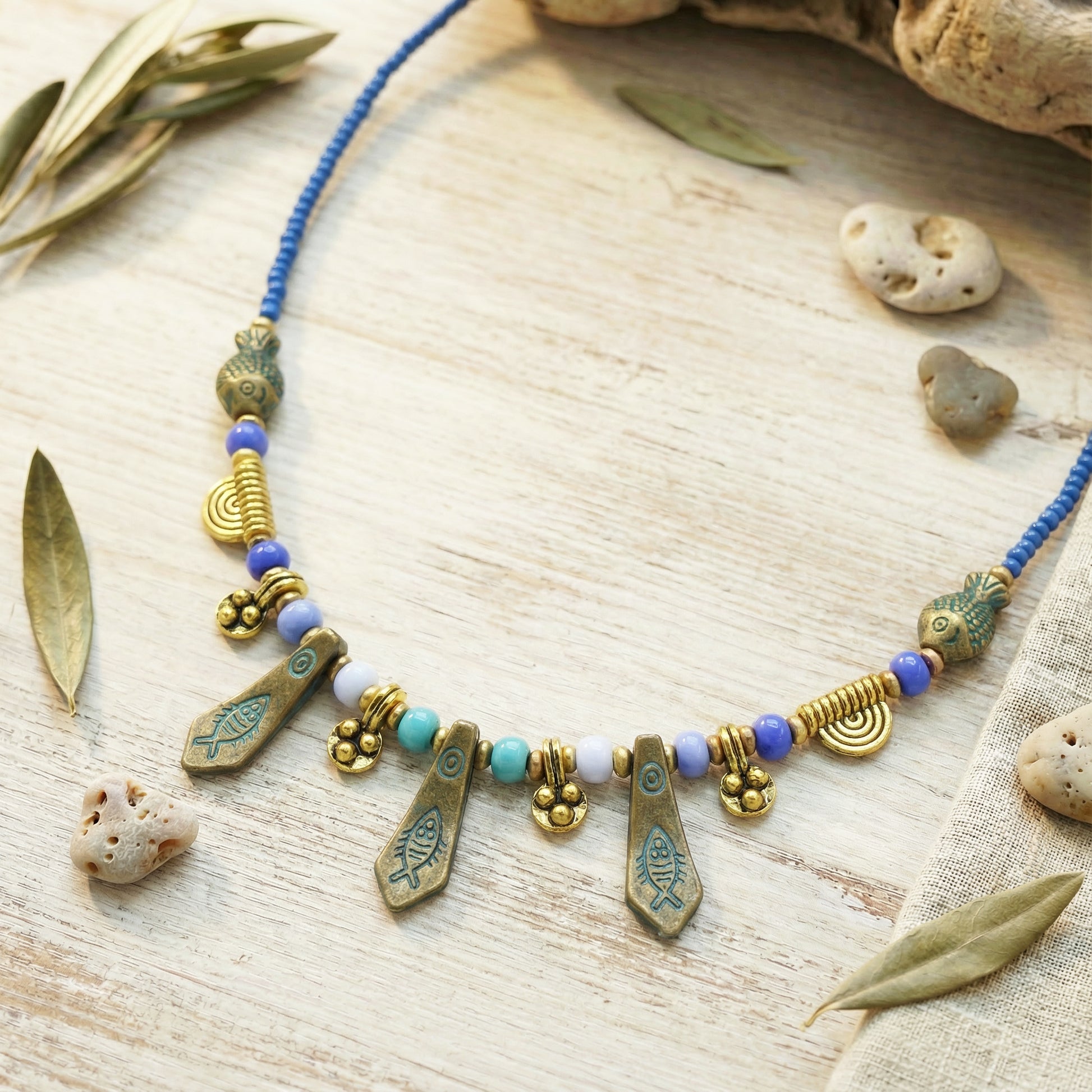 Necklace with gold and blue beads on a wooden surface with leaves and stones