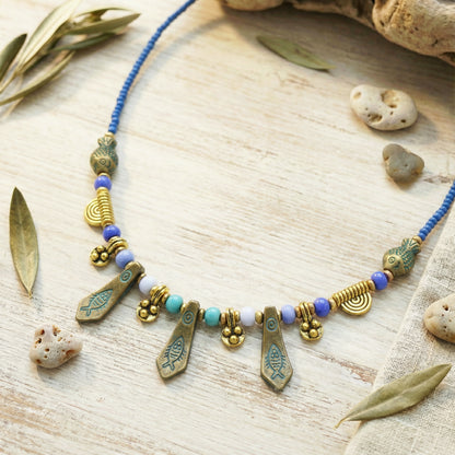 Necklace with gold and blue beads on a wooden surface with leaves and stones