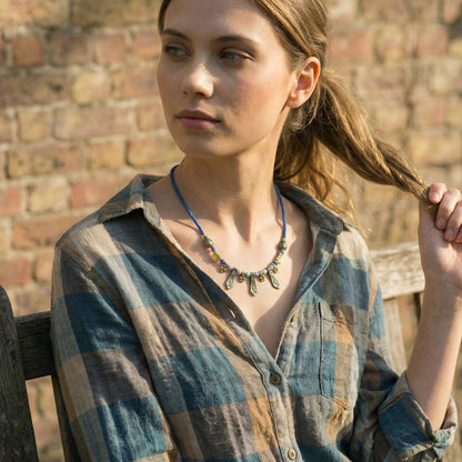 Woman wearing a plaid shirt and colorful necklace against a brick wall.