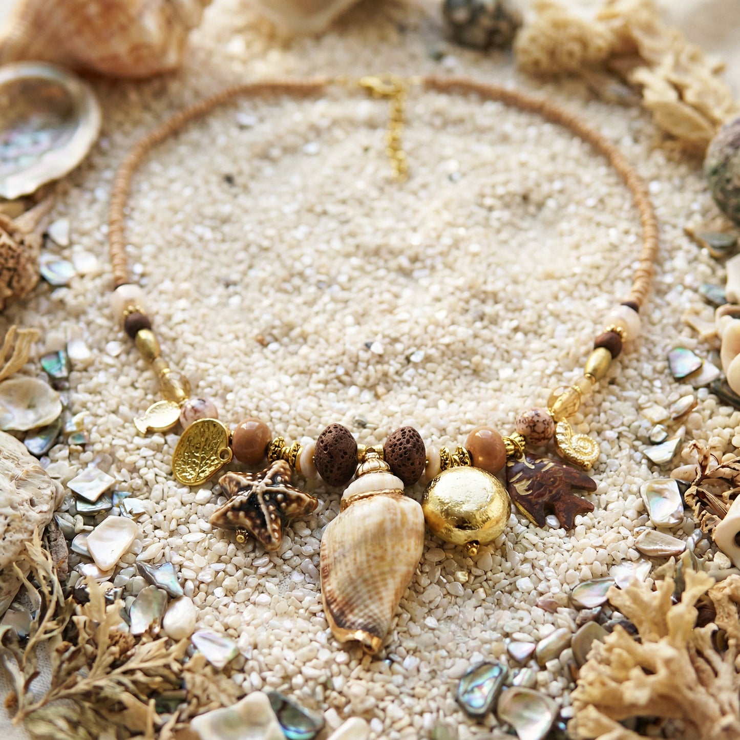 Necklace with seashell and starfish charms on sand and shells