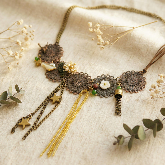 Decorative necklace with floral and star elements on a textured surface with dried flowers and leaves.