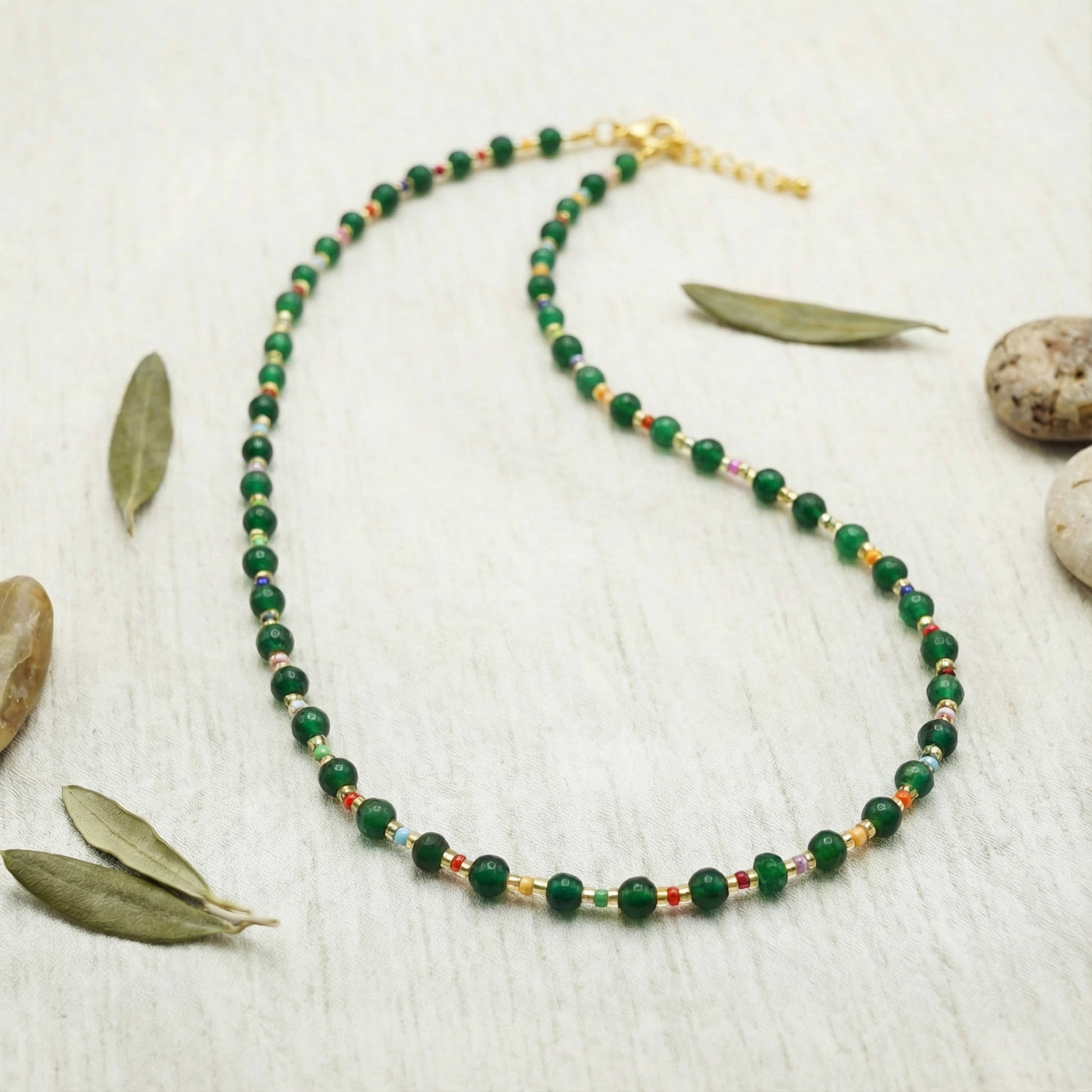 Green beaded necklace on a light wooden surface with leaves and stones.