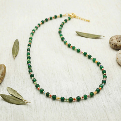 Green beaded necklace on a light wooden surface with leaves and stones.