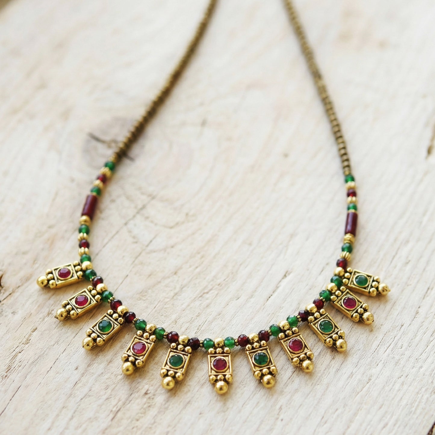 Decorative necklace with gold, green, and red beads on a light wooden surface