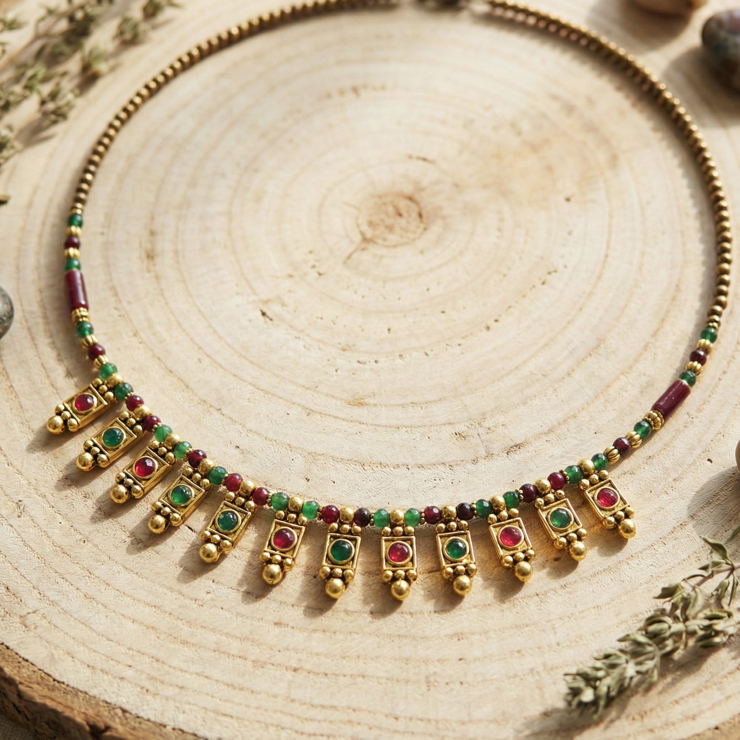 Gold necklace with red and green beads on a wooden surface