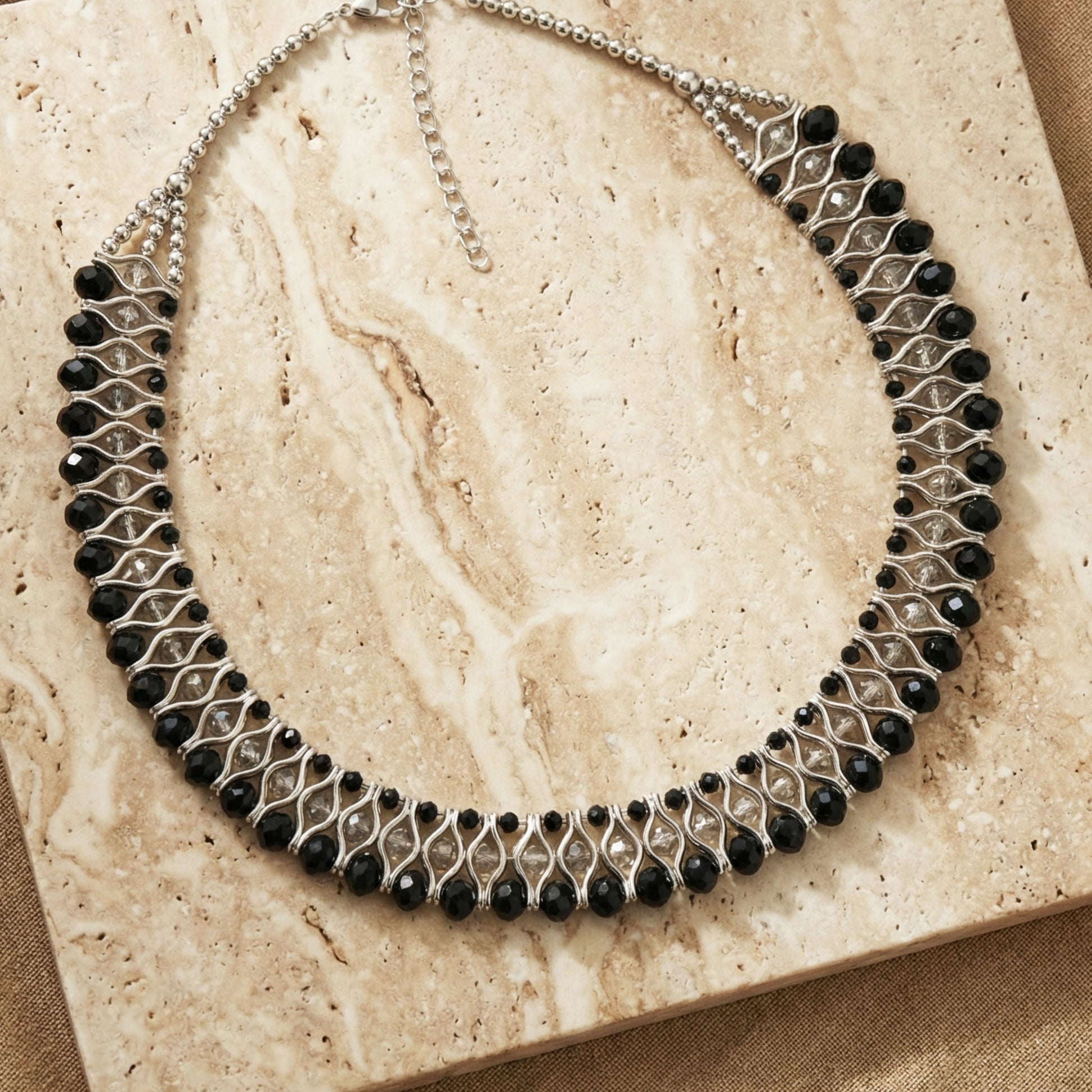 Necklace with black beads and silver chain on a beige stone surface