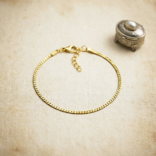 Gold chain bracelet on a textured beige surface with a small decorative box.