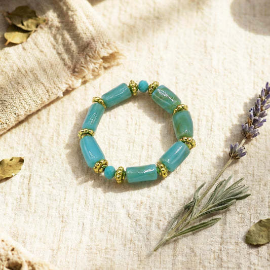Turquoise beaded bracelet with gold accents on a textured beige surface with lavender and herbs.