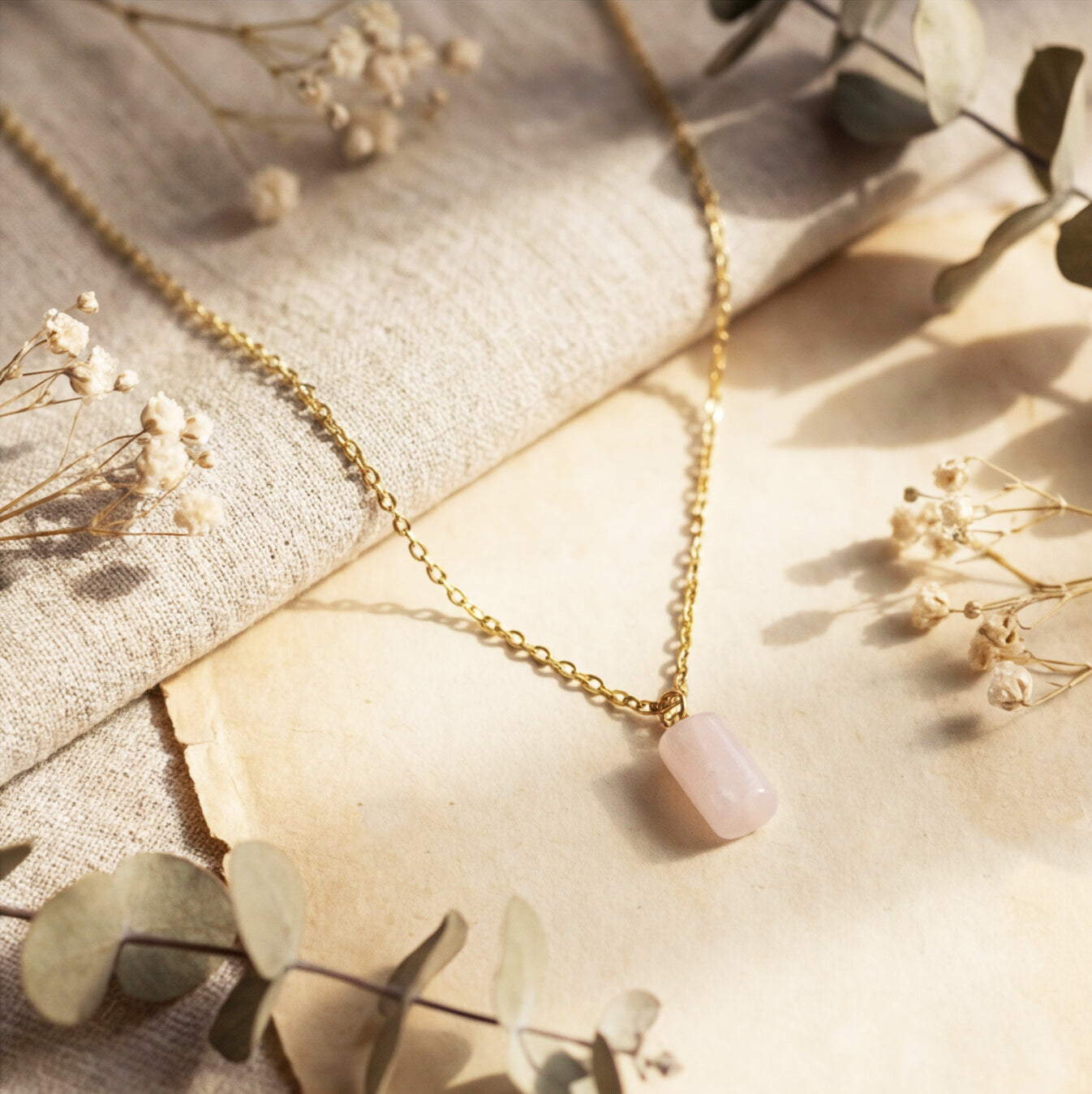 Rose Quartz Necklace on a textured surface with dried flowers.