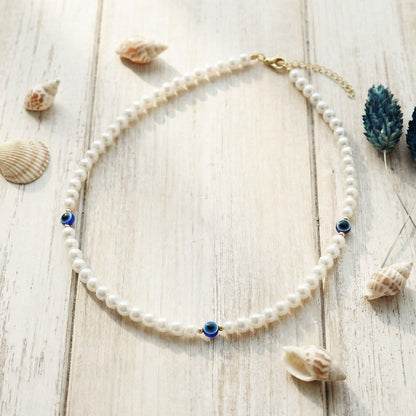 Pearl necklace with blue accents on a wooden surface with seashells and a plant.