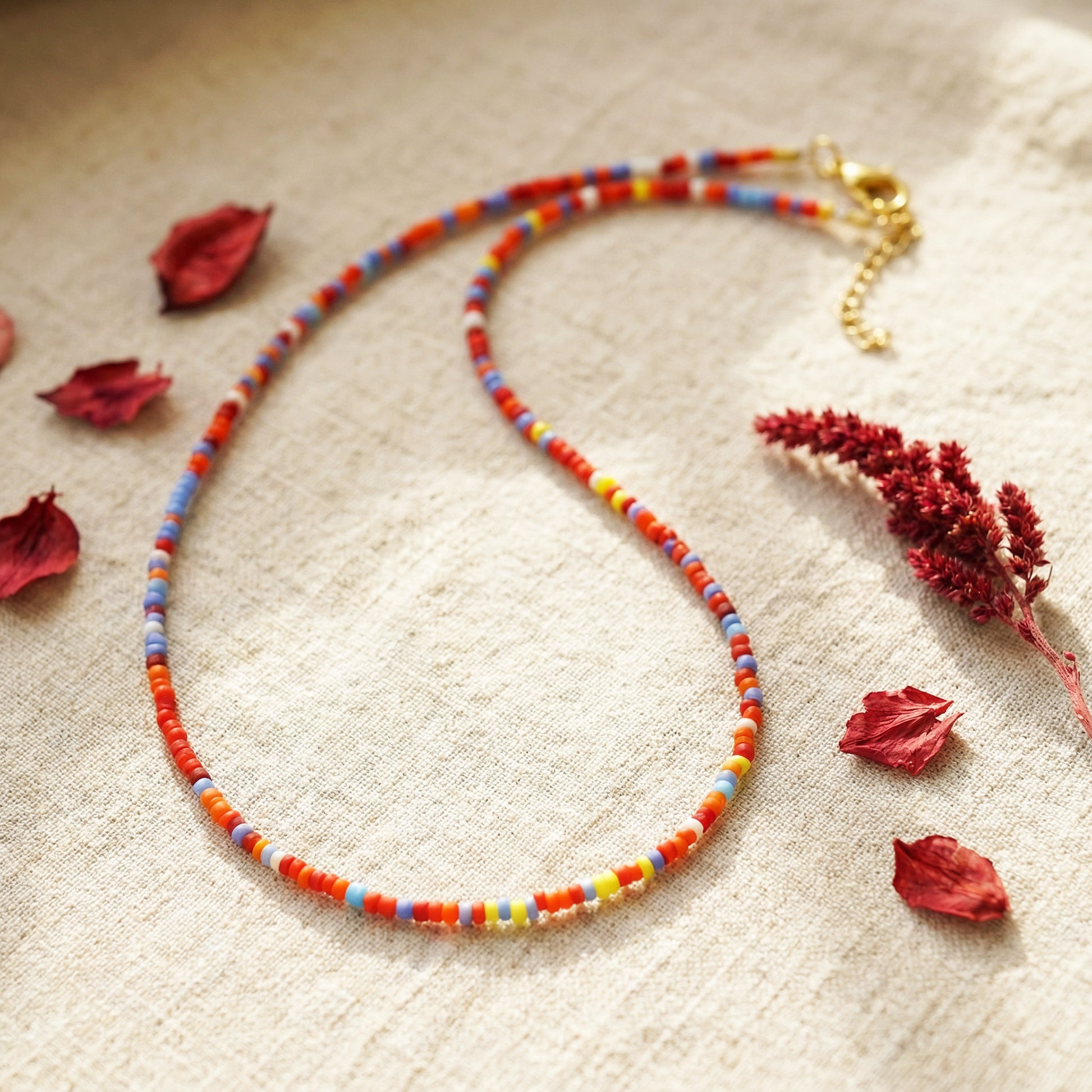 Colorful beaded necklace on a textured surface with dried flowers