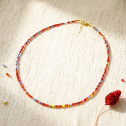 Colorful beaded necklace on a textured surface with a red flower.