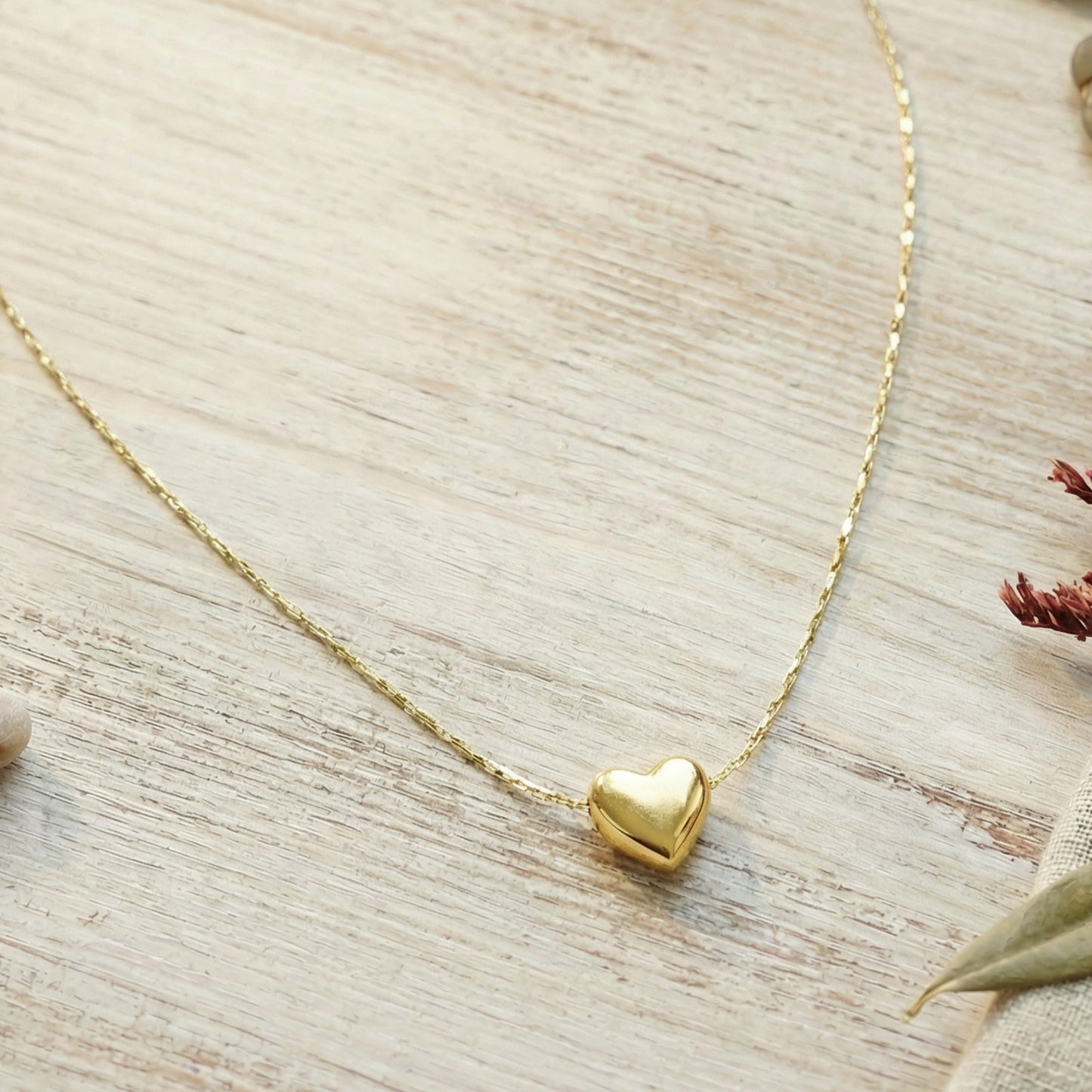 Gold heart-shaped pendant necklace on a light wooden surface