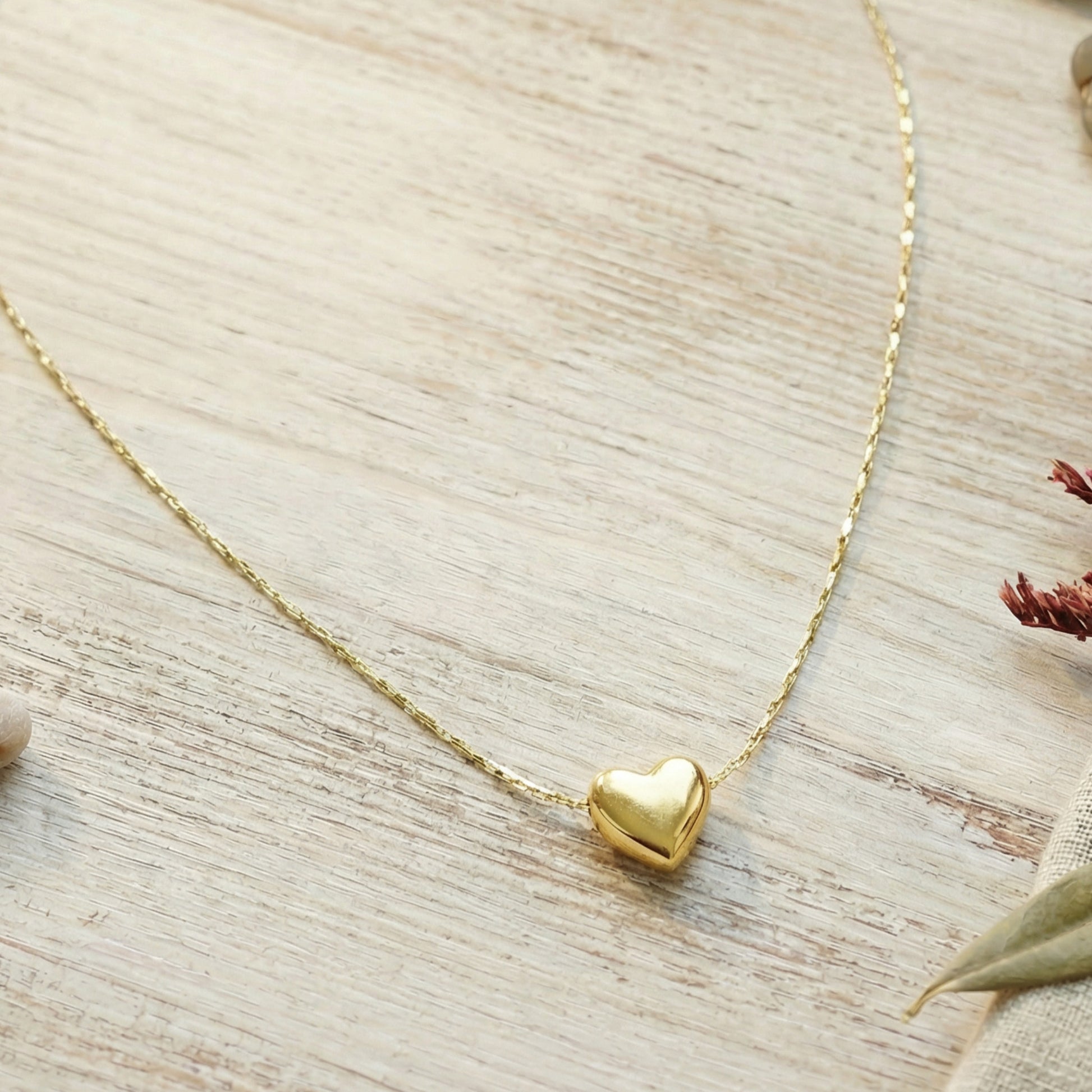 Gold heart-shaped pendant necklace on a light wooden surface