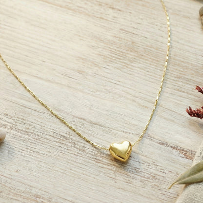 Gold heart-shaped pendant necklace on a light wooden surface