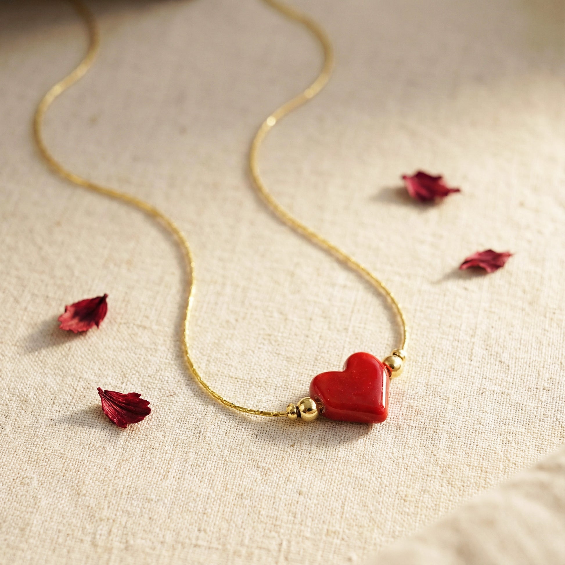 Gold necklace with a red heart pendant on a beige fabric background