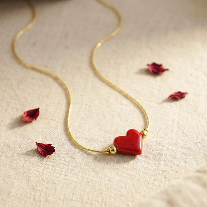 Gold necklace with a red heart pendant on a beige fabric background